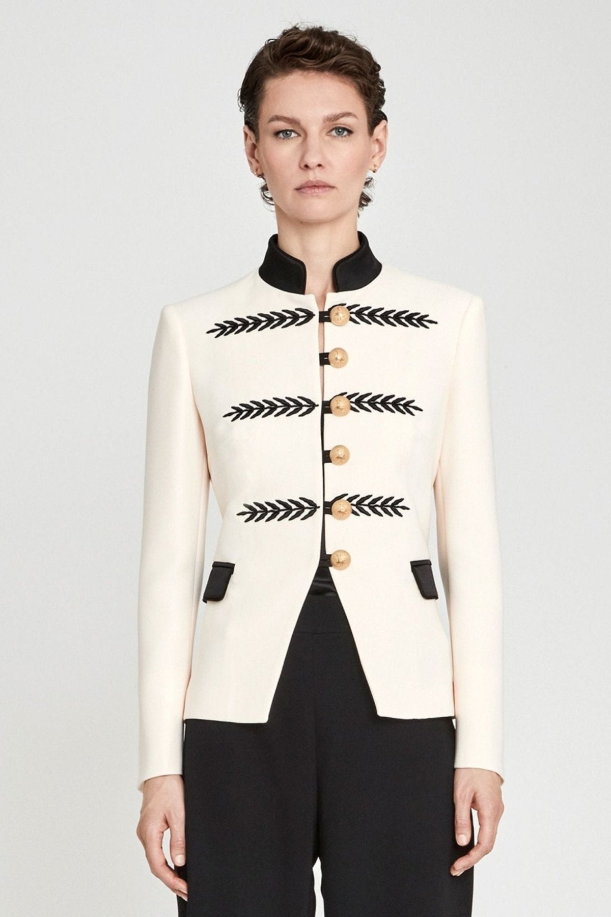 Blazer militar marfil Renata 01 corta y entallada en tejido color crema con cuello mao negro, bordados geométricos y botones dorados. Sastrería de lujo.