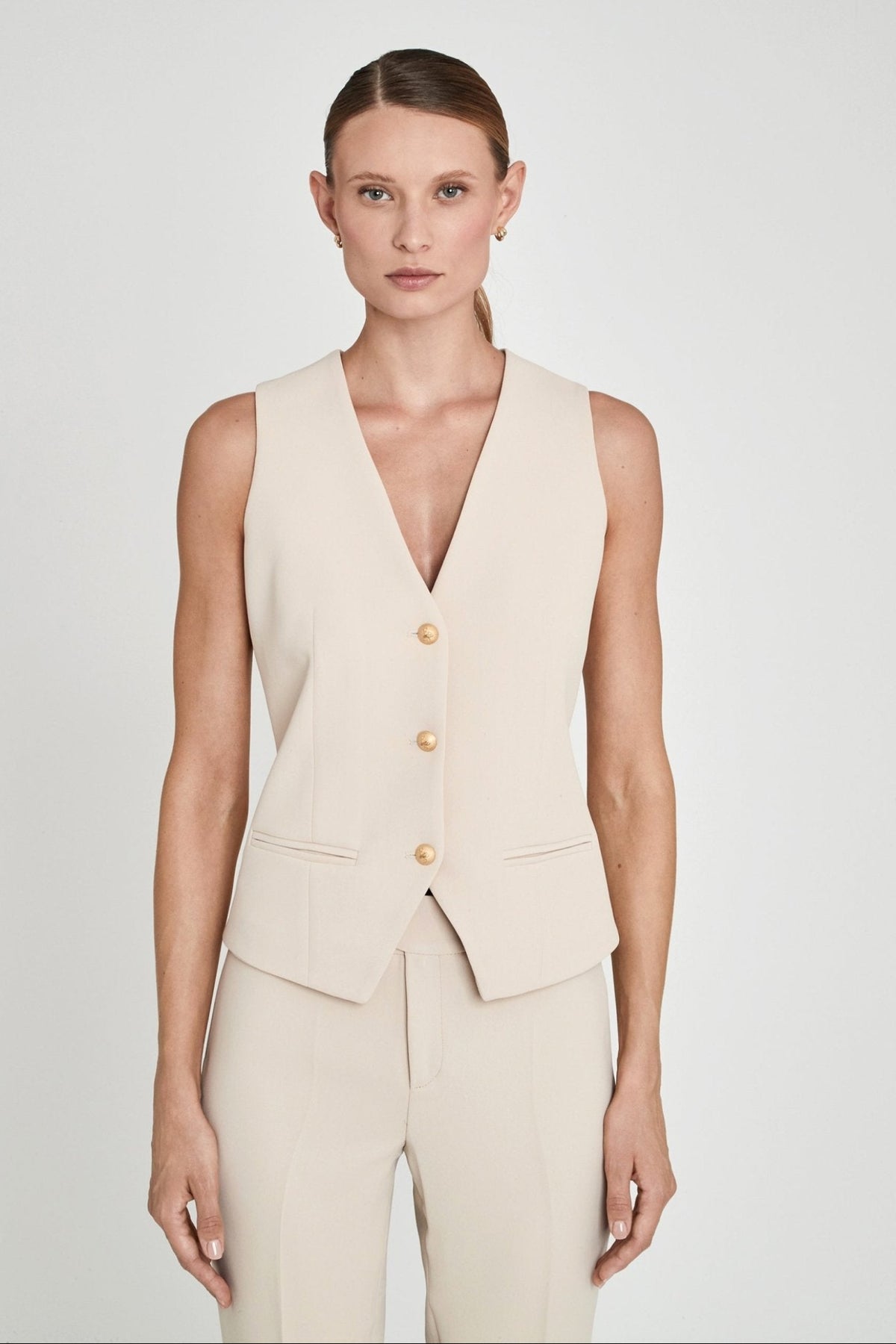 Chaleco sastre beige Atelier en crepe liso en tono tofe con escote en V, tres botones dorados y silueta entallada. Sastrería elegante y sofisticada.