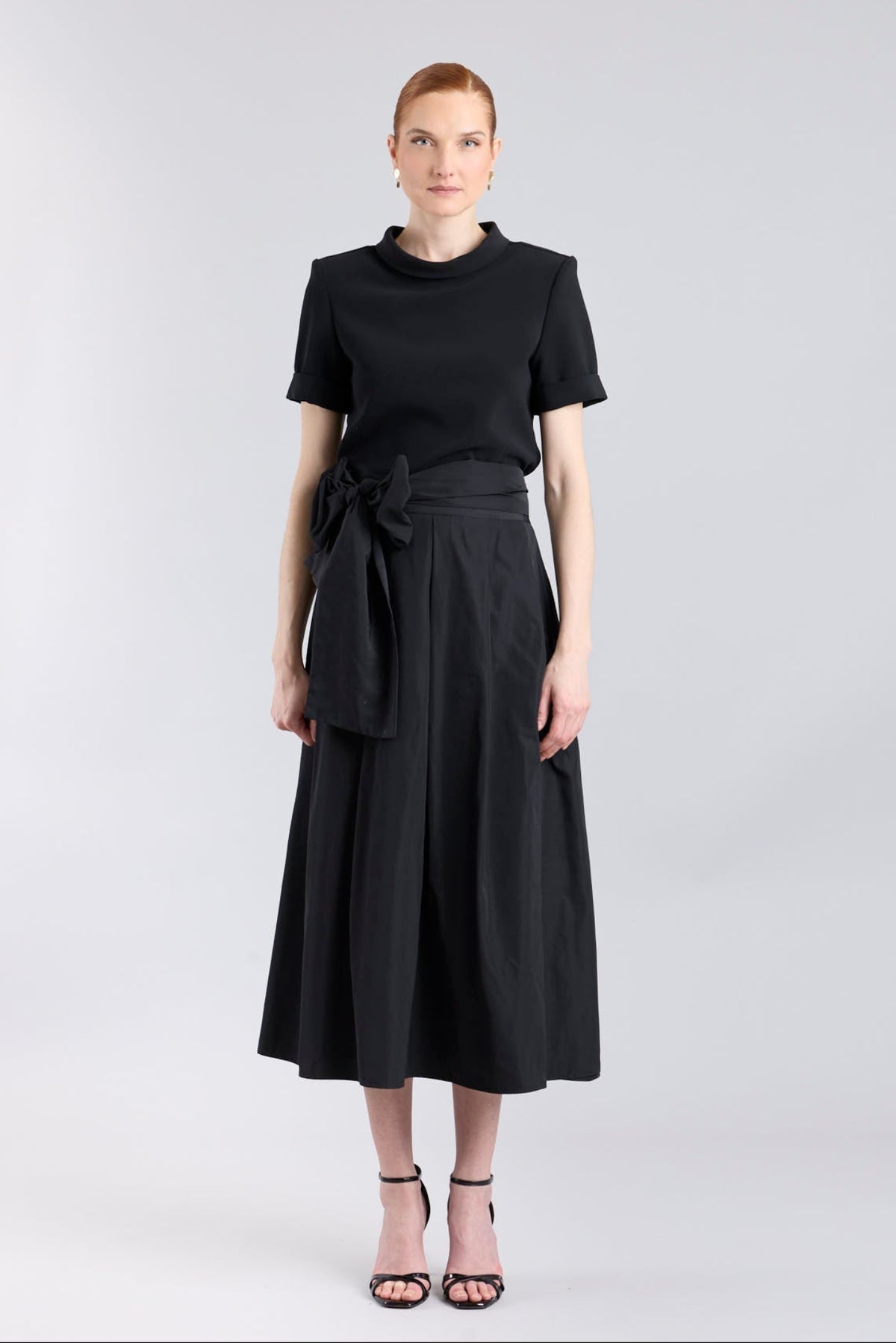 Falda midi negro estructurada con volumen teatral, corte evasé y gran lazo sastre lateral. Alta costura, exclusividad y diseño artesanal hecho en España.